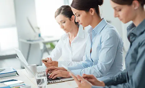 Kolleginnen arbeiten im Büro an Laptops und Smartphones
